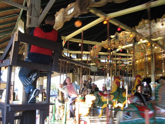 Girl tries to grab brass ring on Balboa Park carousel.