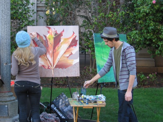 Two artists on El Prado paint colorful canvases.