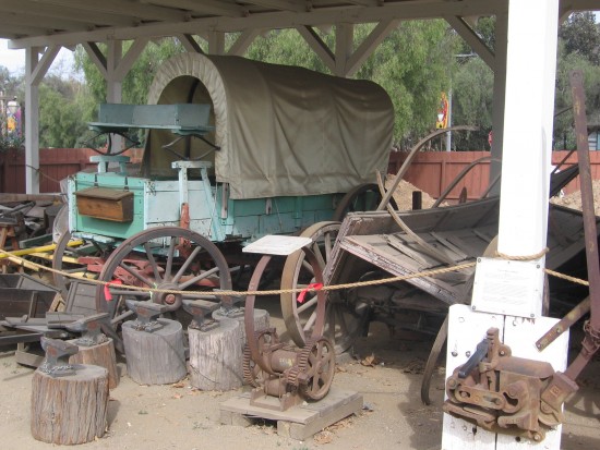 Covered wagon, anvils and relics of the Old West behind Seeley Stable.