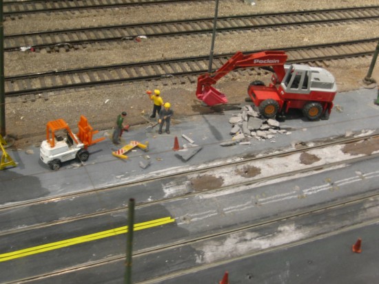 Tiny human figures at work near some trolley tracks.