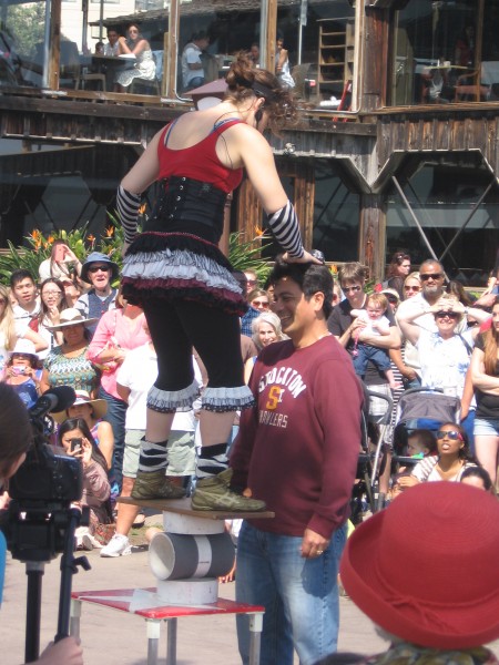 Acrobatic juggler entertains crowd with spectator's help.