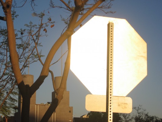 Back of stop sign flashes silver in the morning sunlight.
