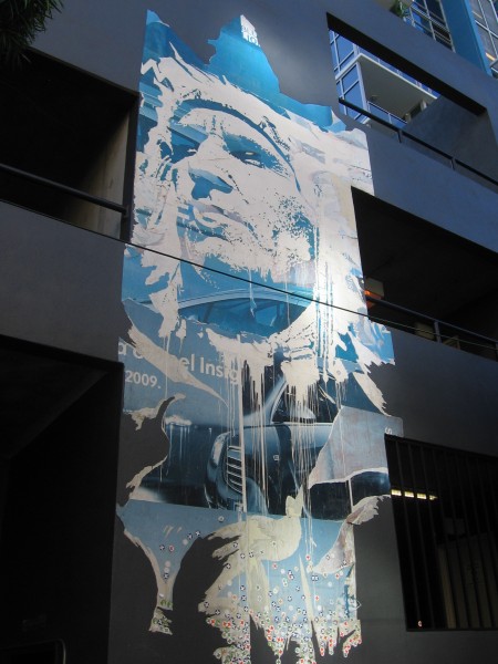 Mural of Native American appears tattered on a modern building.