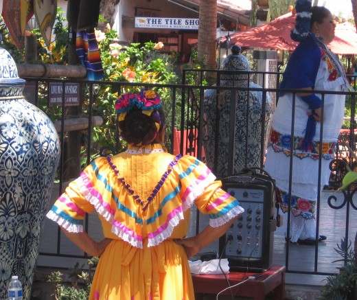 One Mexican folk dancer watches another on stage.