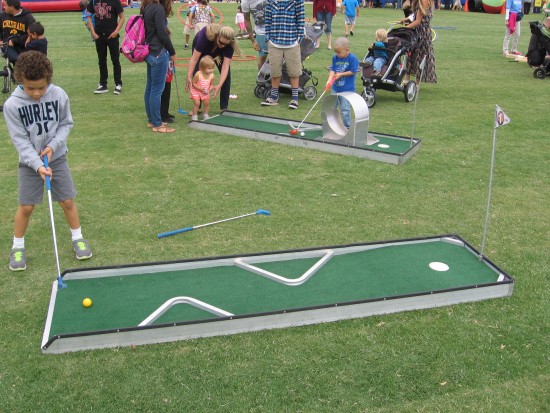 Kids play miniature golf on the grassy lawn.