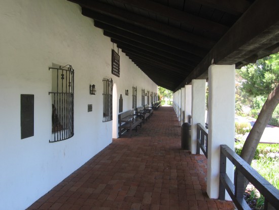 Corridor in front of mission has plaques and statues of saints.