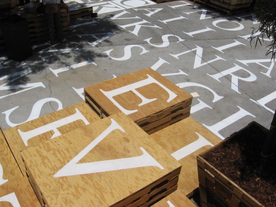 Letters on the ground and pallets form a big word find puzzle.