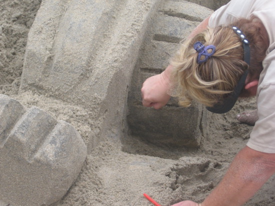 Artist works on a tire of a Transformers sand sculpture.