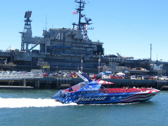 Patriot speed boat leaves dock, passing USS Midway.