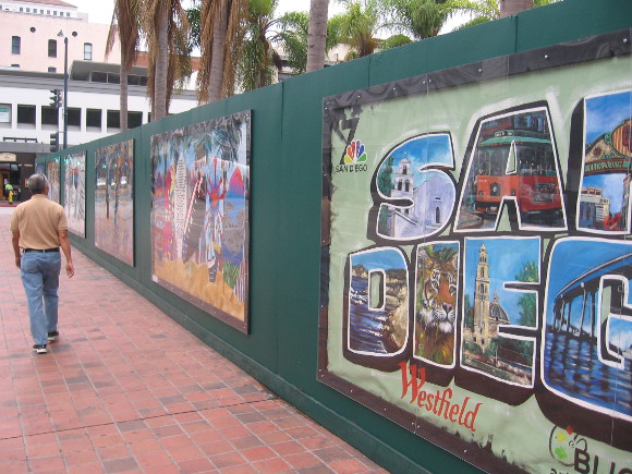Man walks past construction fence surrounding Horton Plaza Park.