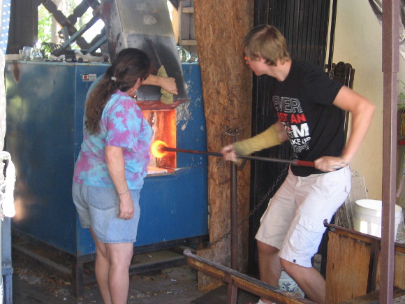Glassblowers in Spanish Village remove red hot molten glass from furnace.