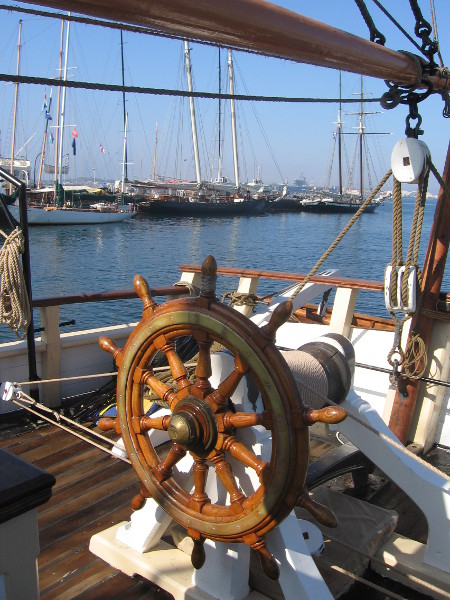 Beyond ship's wheel, several tall ships are docked at Maritime Museum.