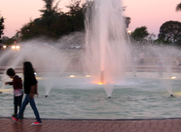Children walk around Balboa Park fountain as evening descends.