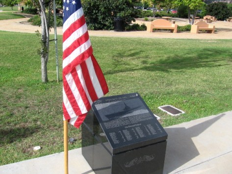 American flag shelters one of the solemn black marble markers.