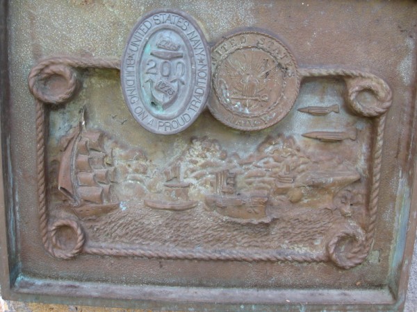 Corroded plaque shows tallship, ironclad, early warship, aircraft carrier and jets.