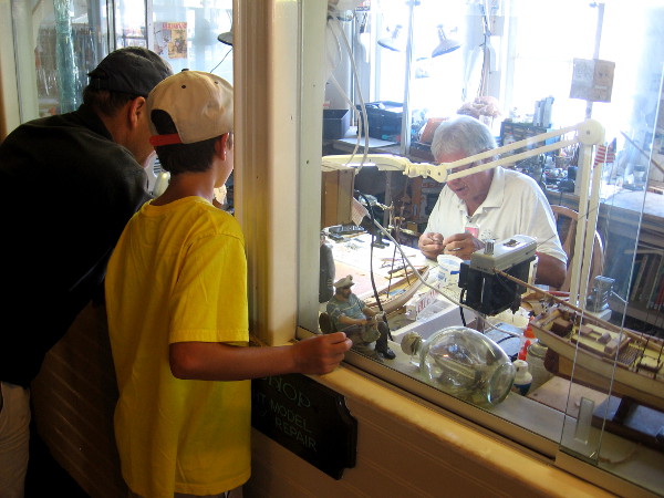 Inside the Berkeley a family watches a hobbyist create a tiny ship model.