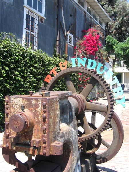 Rusted factory gears on sidewalk with words Art and Industry.