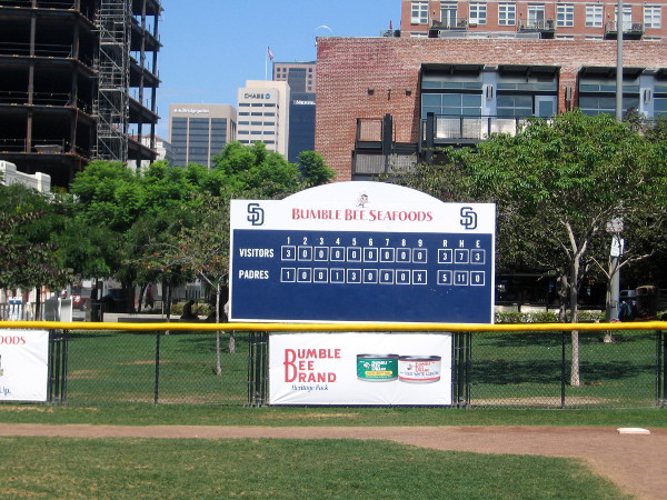 Scoreboard beyond outfield of tiny baseball diamond sponsored by Bumble Bee.