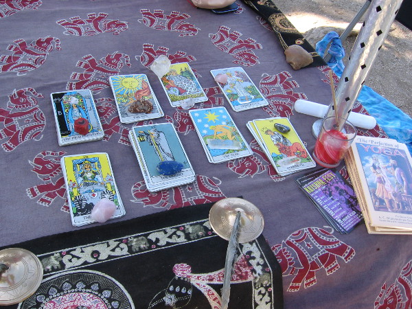 Table next to sidewalk features tarot cards kept in place by crystal paperweights.