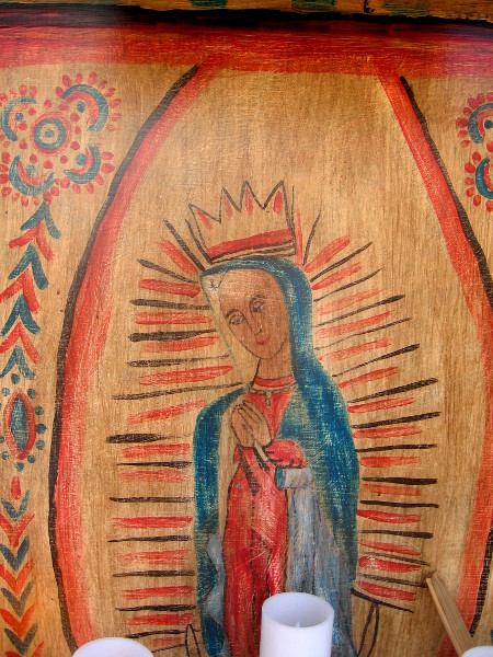 Radiant image of Virgin Mary on wood above altar candles.