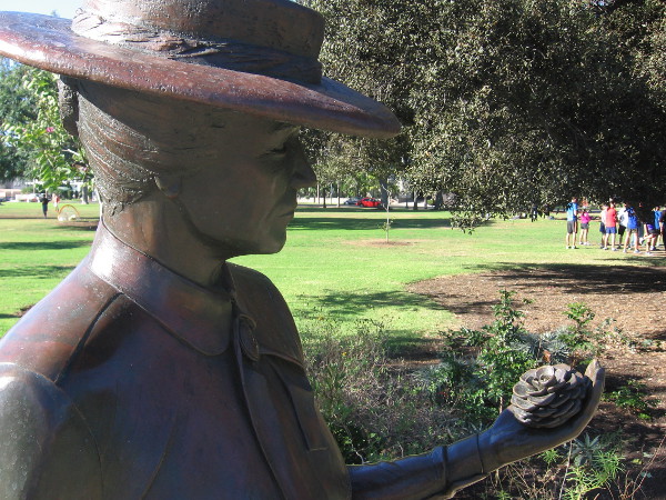 Kate Sessions, the Mother of Balboa Park, holds a pine cone by the grass.