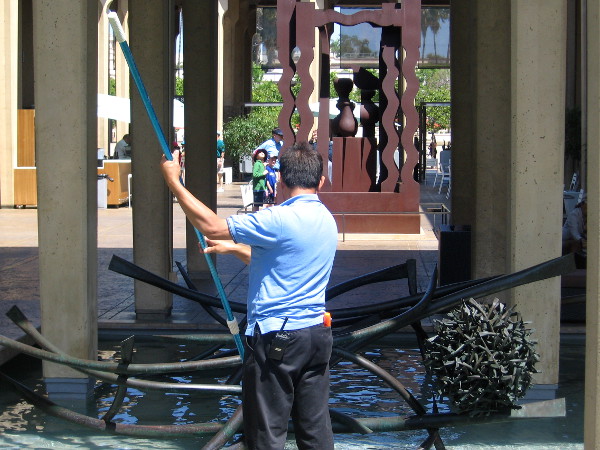 Man cleans pool of water in San Diego Museum of Art's Sculpture Court.