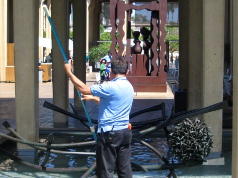 Man cleans pool of water in San Diego Museum of Art's Sculpture Court.