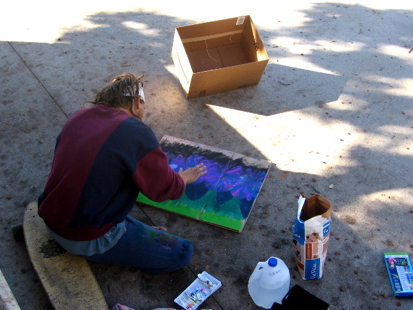 Young man with skateboard paints for donations on a San Diego sidewalk.