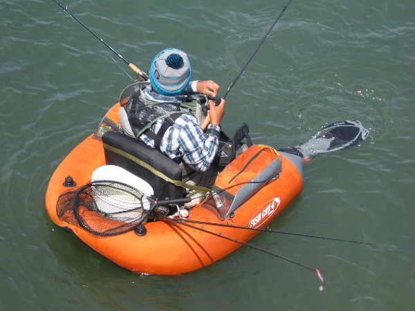 Guy in small inflatable with bucket, net and fishing rods hopes to catch something.