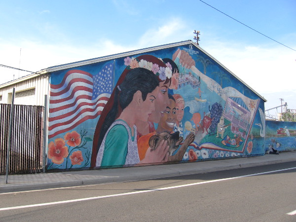 Fun mural in Barrio Logan shows flag, kids, fruit, a train and birds.
