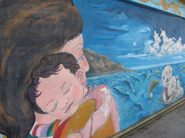 Mother with young child gazes out at the blue Pacific Ocean.