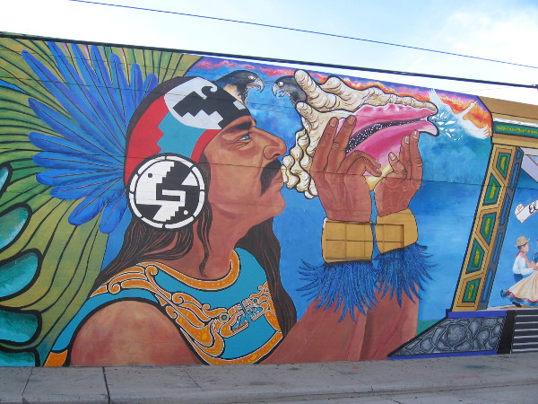 Aztec warrior in elaborate costume blows on a ceremonial conch.