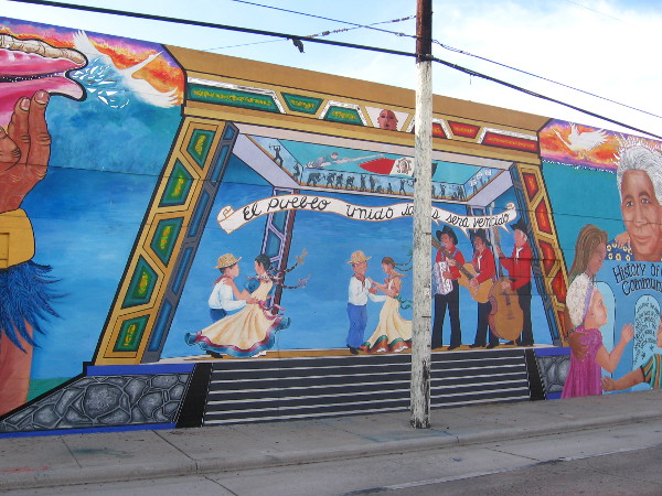 Nearby Chicano Park's pavilion is shown with lots of folks dancing.