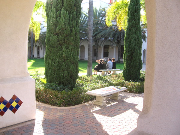 Some people rest on a bench in the sunny courtyard.