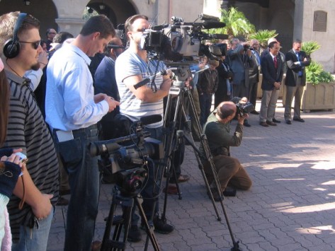 News cameras wait for speeches, and so do the assembled dignitaries nearby.