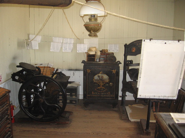 Massive Washington hand press can be glimpsed to the right in small printing shop.