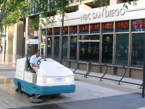 Man cleans sidewalk in early morning at downtown NBC building.