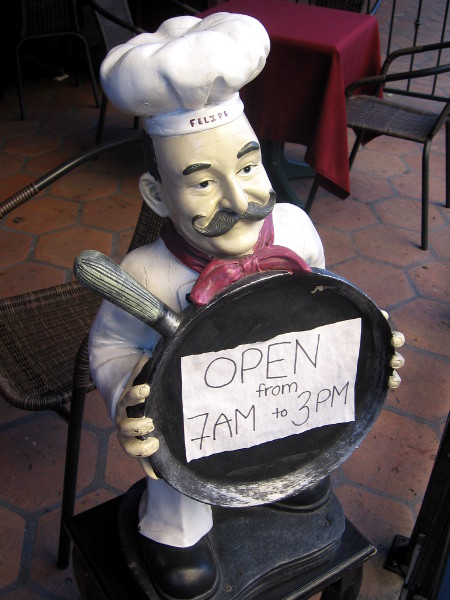 Chef carries a frying pan outside on a downtown San Diego sidewalk.