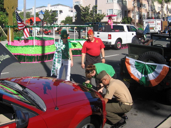Serviceman helps affix some green to the front bumper of a car.