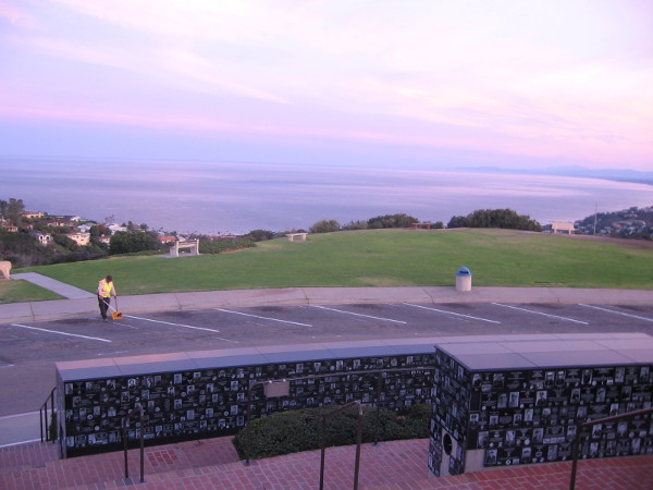 Gazing over curved walls containing memorial plaques toward the Pacific Ocean in morning light.