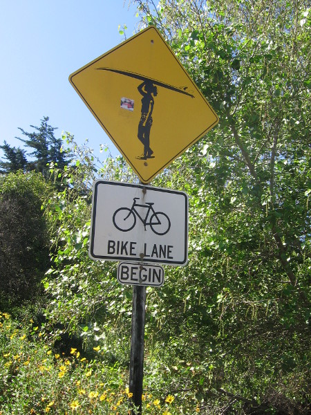 Surfer crossing sign on Pacific Coast Highway near trail to Moonlight Beach.