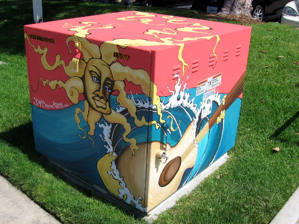 Electrical transformer box decorated with sun, surf and guitar.