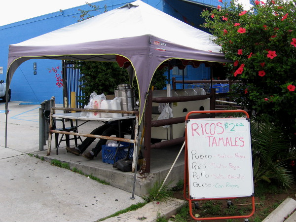 Local vendor is selling tamales under a canopy by the sidewalk.