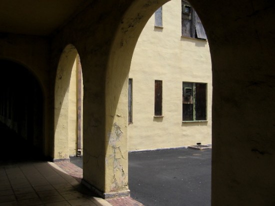 Photo of shuttered windows taken through dark, weathered archway.