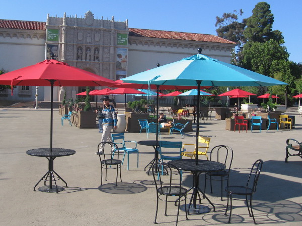 People mix with red and blue umbrellas in the big square in front of the San Diego Museum of Art.