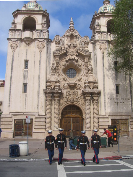 Marines cross street in front of the Casa del Prado Theatre building.