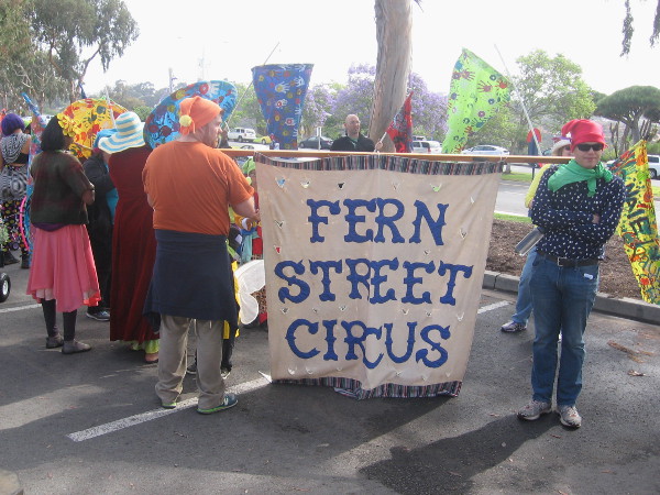 San Diego's own Fern Street Circus has gathered for the parade holding colorful banners.
