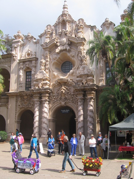Flower-laden wagons pass in front of ornate Casa del Prado.