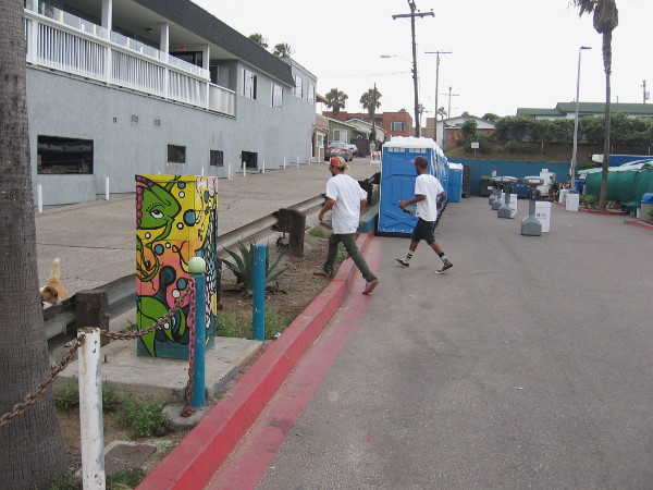 Some guys walking along near porta-potties by the beer garden.