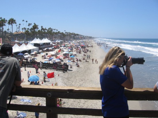 Camera aims toward surfing action from the Oceanside Pier during 2015 Supergirl Pro World Surf League (WSL) competition.